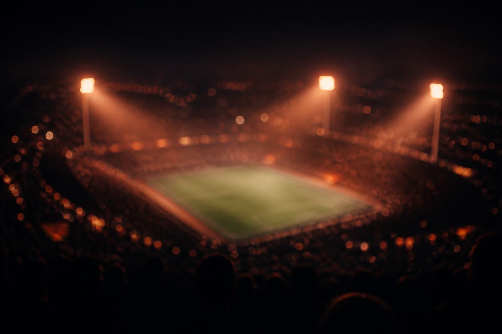 Floodlit stadium at night seen from the upper stands, deliberately out of focus